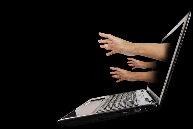 Hand reach out from laptop screen, isolated on black background